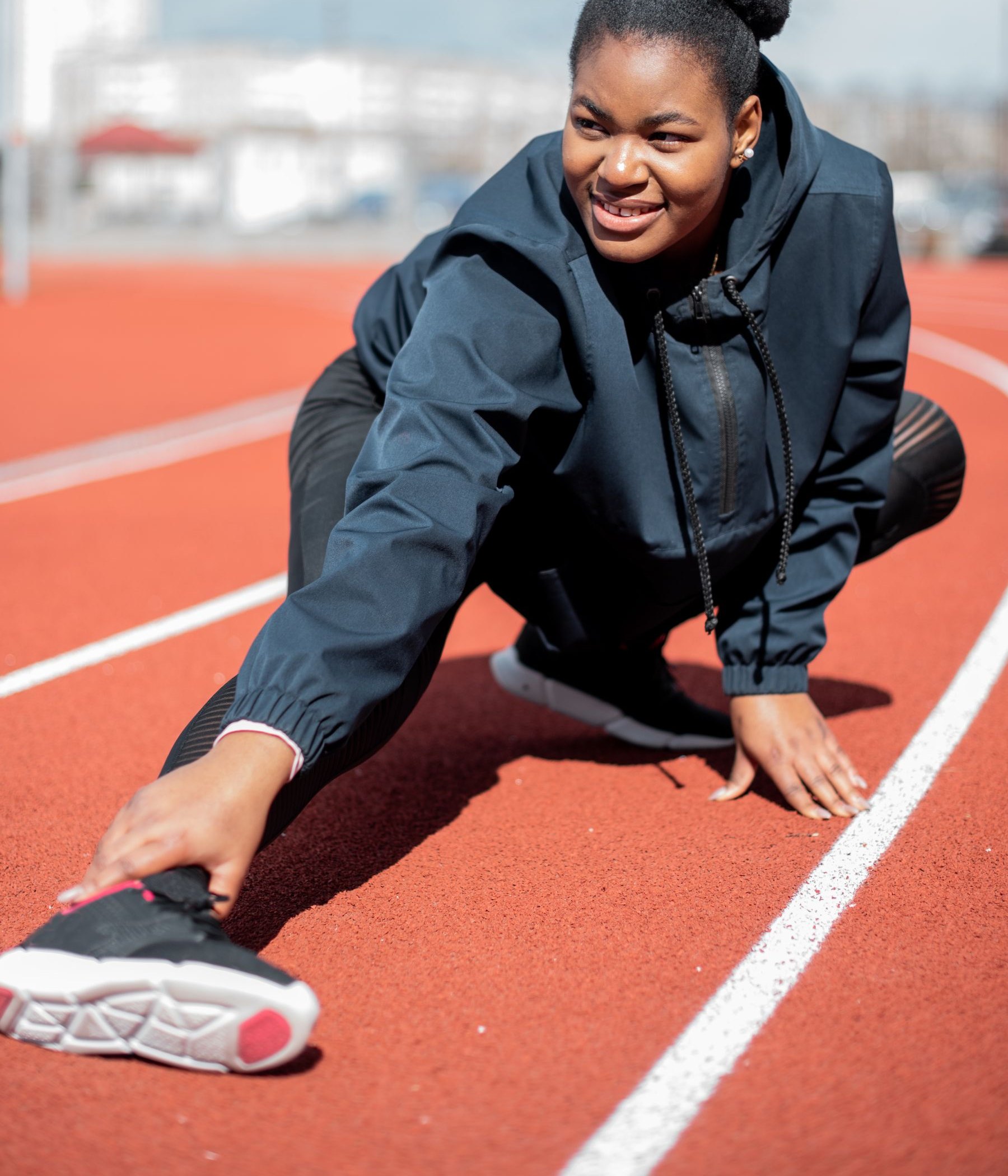 Athlete on a running track with one leg extended, loading the hamstring at length