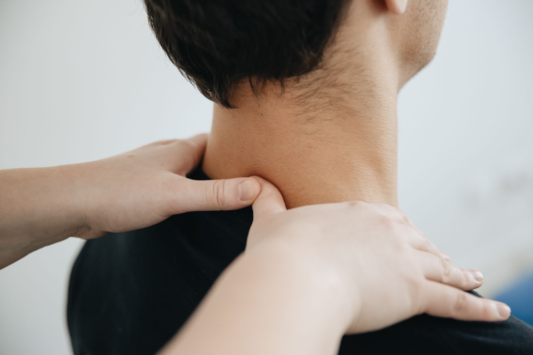 Therapist's hands assessing the suboccipital muscles at the base of the skull, a common source of referred headache pain