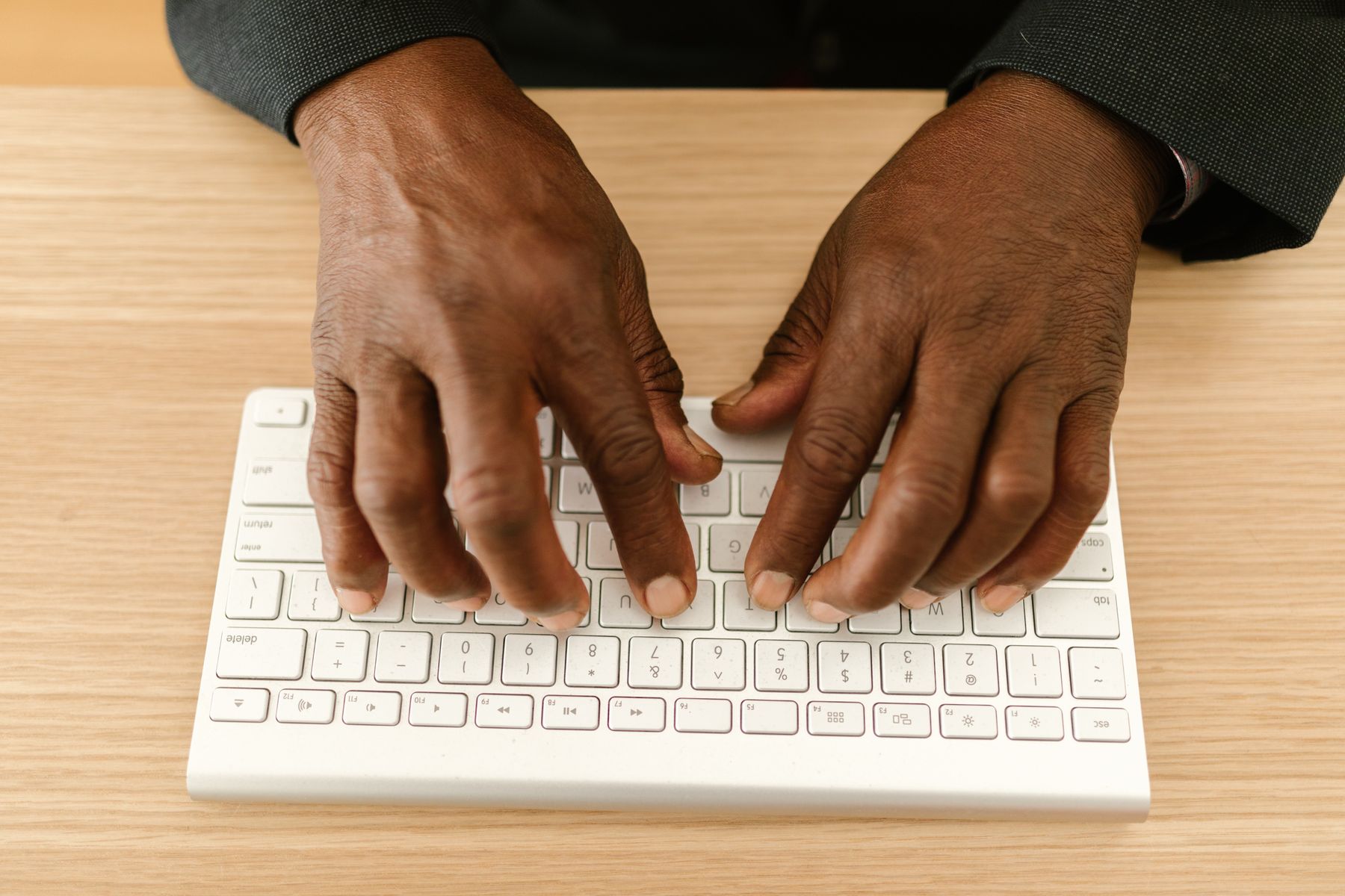 Hands typing at a keyboard on a wooden desk