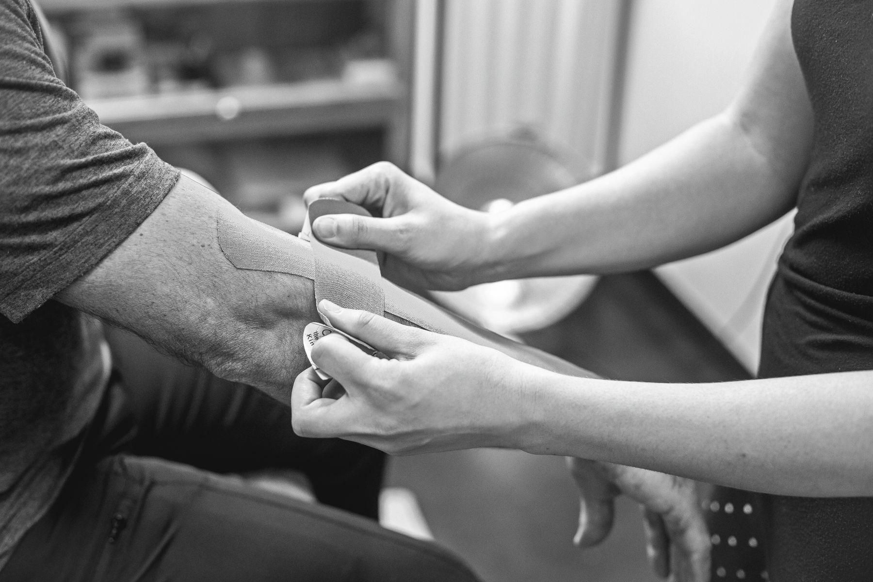 Therapist applying kinesiology tape to a patient's forearm and elbow