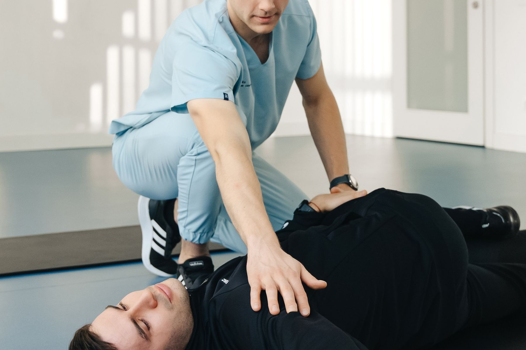 Doctor of Physical Therapy guiding a patient through post-operative exercise on a mat